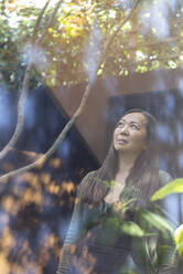 Thoughtful mature woman looking up at tree in courtyard - CAIF33213