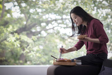 Young woman eating lunch with chopsticks at home - CAIF33221