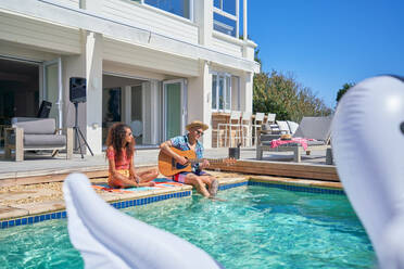 Ehepaar entspannt sich und spielt Gitarre am sonnigen Swimmingpool eines Luxushauses - CAIF33269