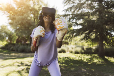 Elderly woman with VR Goggles boxing in public park - JCCMF06530