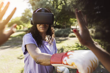 Lächelnde Seniorin beim Boxen mit dem Virtual-Reality-Simulator ihrer Tochter im Park - JCCMF06531