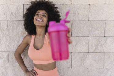 Lächelnde Afro-Frau zeigt Wasserflasche aufheben - JCCMF06538