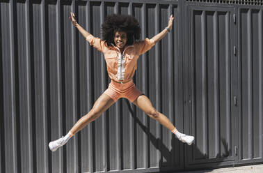 Cheerful Afro sports woman jumping in front of black wall - JCCMF06567