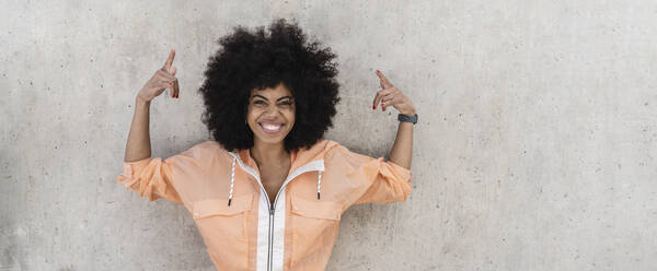 Happy Afro sports woman gesturing in front of wall - JCCMF06569