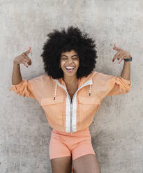 Afro woman laughing and gesturing in front of wall - JCCMF06570