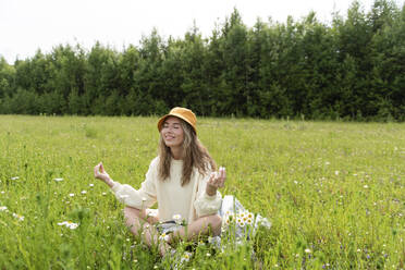 Lächelnde Frau, die mit geschlossenen Augen bei Kamillenblüten sitzt - VBUF00133