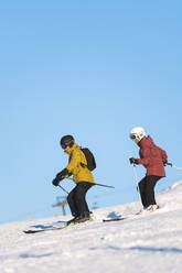 Couple skiing by blue sky in resort, Baqueira Beret, Pyrenees, Spain - JAQF01036