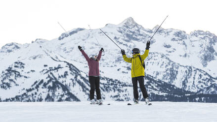 Pärchen mit Skistöcken vor einem schneebedeckten Berg, Baqueira Beret, Pyrenäen, Spanien - JAQF01040