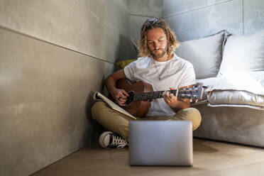 Man e-learning guitar through laptop in living room - DLTSF02967