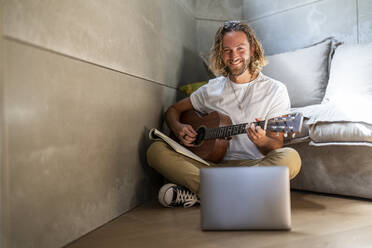 Smiling composer playing guitar at home - DLTSF02968