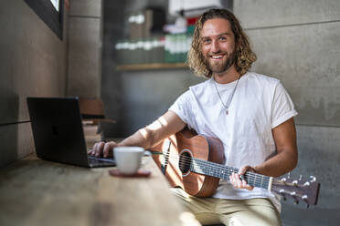 Glücklicher Komponist, der zu Hause über seinen Laptop Gitarre lernt - DLTSF02971