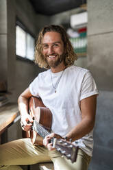 Smiling guitarist playing guitar at home - DLTSF02972