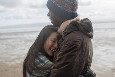 Happy affectionate couple hugging on winter beach - CAIF33303
