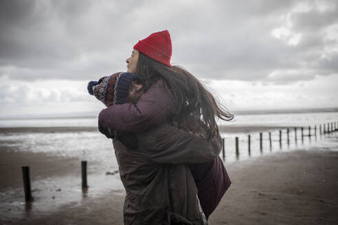 Happy affectionate couple hugging on wet winter beach - CAIF33311
