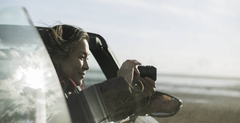 Woman with digital camera in convertible on winter beach - CAIF33324