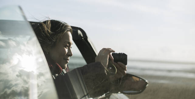 Frau mit Digitalkamera im Cabrio am Winterstrand - CAIF33324