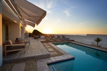 Sunset over ocean behind modern, luxury patio swimming pool - CAIF33331