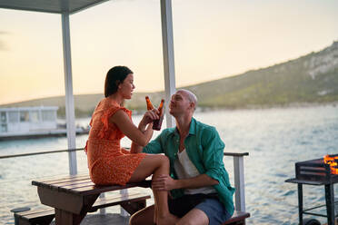 Happy couple drinking beers on houseboat patio - CAIF33347