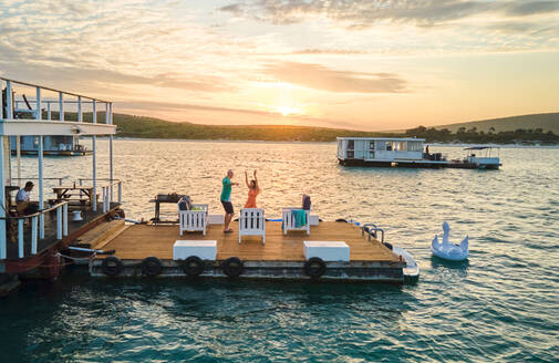 Unbeschwertes Paar tanzt auf der Terrasse eines Hausboots auf dem See bei Sonnenuntergang - CAIF33354