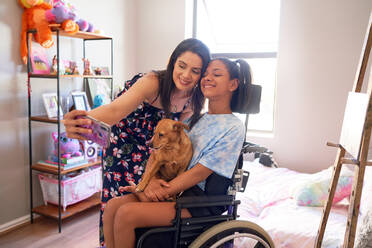 Glückliche Mutter und behinderte Tochter mit Hund machen Selfie zu Hause - CAIF33365