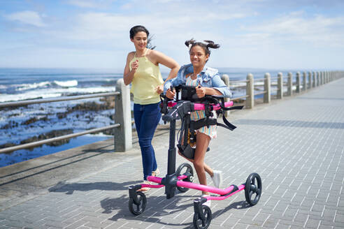 Mutter und behinderte Tochter mit Rollator joggen auf der Strandpromenade - CAIF33376