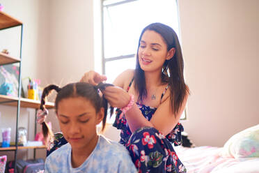 Mother braiding daughter's hair into pigtails in bedroom at home - CAIF33377