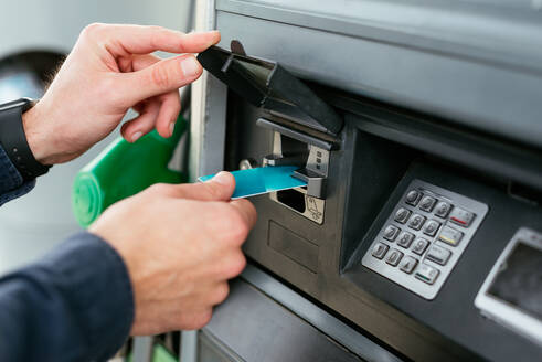 Abgeschnittene, nicht erkennbare Person, die mit Karte an einem Automaten in einer modernen Tankstelle bezahlt - ADSF34866