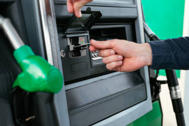 Abgeschnittene, nicht erkennbare Person, die mit Karte an einem Automaten in einer modernen Tankstelle bezahlt - ADSF34867