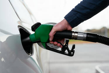 Cropped unrecognizable man refilling vehicle tank at petrol station during energy crisis - ADSF34868