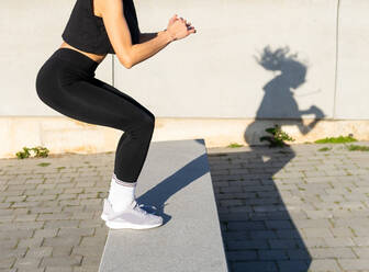 Crop anonyme sportliche Frau in schwarzer Sportkleidung springen auf Grenze während Fitness-Training in der Stadt auf Sommer sonnigen Tag - ADSF34906