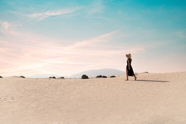 Junge Touristin, die auf einem Sandhügel spazieren geht, während sie die Dünen von Corralejo bei Sonnenuntergang auf Fuerteventura (Kanarische Inseln) erkundet - ADSF34920