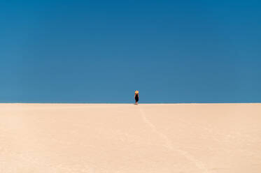 Junge Touristin, die auf einem Sandhügel spazieren geht, während sie die Dünen von Corralejo unter blauem Himmel auf den Kanarischen Inseln von Fuerteventura erkundet - ADSF34926