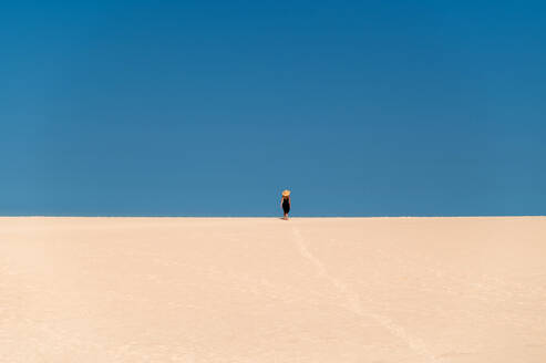 Junge Touristin, die auf einem Sandhügel spazieren geht, während sie die Dünen von Corralejo unter blauem Himmel auf den Kanarischen Inseln von Fuerteventura erkundet - ADSF34926