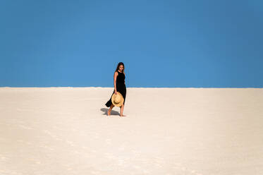 Junge Touristin, die auf einem Sandhügel spazieren geht, während sie die Dünen von Corralejo unter blauem Himmel auf den Kanarischen Inseln von Fuerteventura erkundet - ADSF34927