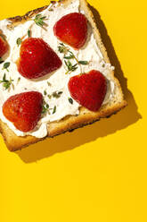 Draufsicht auf leckere Toasts mit Frischkäse und reifen Erdbeeren, dekoriert mit Grünzeug auf gelbem Hintergrund - ADSF34937