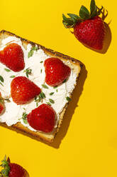 Draufsicht auf leckere Toasts mit Frischkäse und reifen Erdbeeren, dekoriert mit Grünzeug auf gelbem Hintergrund - ADSF34938