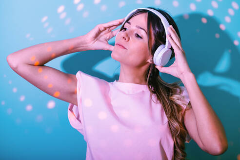 Attraktive Frau hört Musik mit drahtlosen Kopfhörern auf blauem Hintergrund in einem Studio mit hell leuchtenden Lichtern - ADSF34966