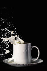Ceramic mug on plate with flying splashes of milk on table against black background - ADSF35011