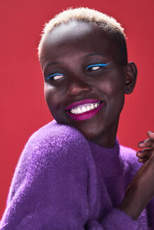 Nahaufnahme einer fröhlichen afrikanischen Frau mit kurzen Haaren in einer Studioaufnahme mit rotem Hintergrund - ADSF35018