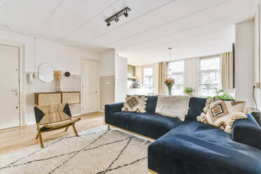 Bequemes Sofa auf Teppich neben Sessel gegen Wand und Schrank mit Blumen in hellem stilvollen Wohnzimmer mit dekorativen Rahmen platziert - ADSF35050