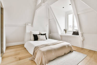 Bequemes Bett mit weißer Decke und Kissen im hellen geräumigen Schlafzimmer - ADSF35065