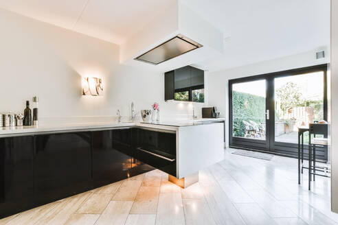 Theke mit schwarzen Schränken und Spüle an weißer Wand in stilvoller geräumiger Küche mit Glastüren in heller Wohnung - ADSF35078
