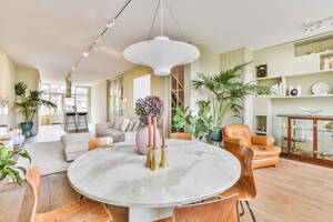 Round table with flowers and candlesticks placed in stylish light living room with couch and green potted plants in apartment - ADSF35096