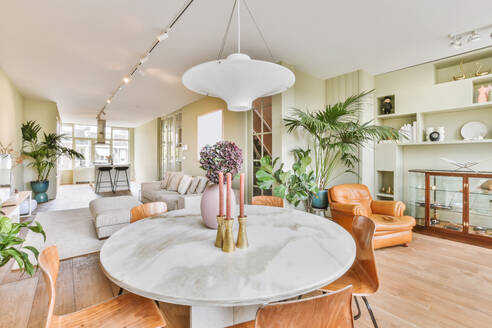 Runder Tisch mit Blumen und Kerzenleuchtern in einem stilvollen hellen Wohnzimmer mit Sofa und grünen Topfpflanzen in einer Wohnung - ADSF35096