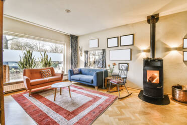 Bequeme Sofas in der Nähe des Teppichs im hellen, geräumigen Wohnzimmer mit Ofen und dekorativen Rahmen in der Wohnung mit Panoramafenster - ADSF35125