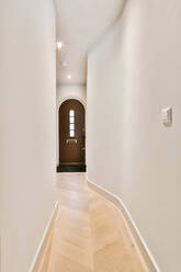 Empty narrow corridor with parquet floor and white walls leading to wooden entrance door in modern apartment - ADSF35130