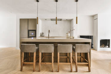 Bequeme Holzstühle mit weicher Sitzfläche an der Theke mit Spüle in einer geräumigen Küche mit minimalistischer Einrichtung und modernen Geräten - ADSF35133