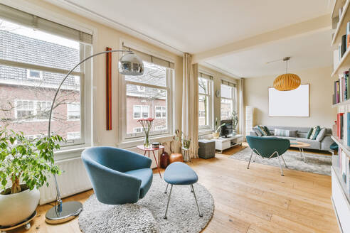 Comfortable couch and armchair placed near windows on rugs in light spacious living room with lamp and modern TV in apartment - ADSF35145