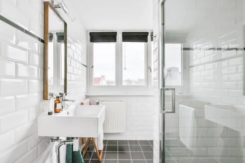 Seitenansicht eines Badezimmers mit hell gefliesten Wänden, Waschbecken und Spiegel und im Hintergrund ein Fenster mit einem Laden - ADSF35164