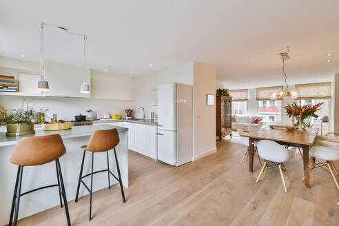 Modern kitchen with island next to a wooden dining table with modern chairs and in the background a living room with sofas near the windows in an open floor plan - ADSF35169